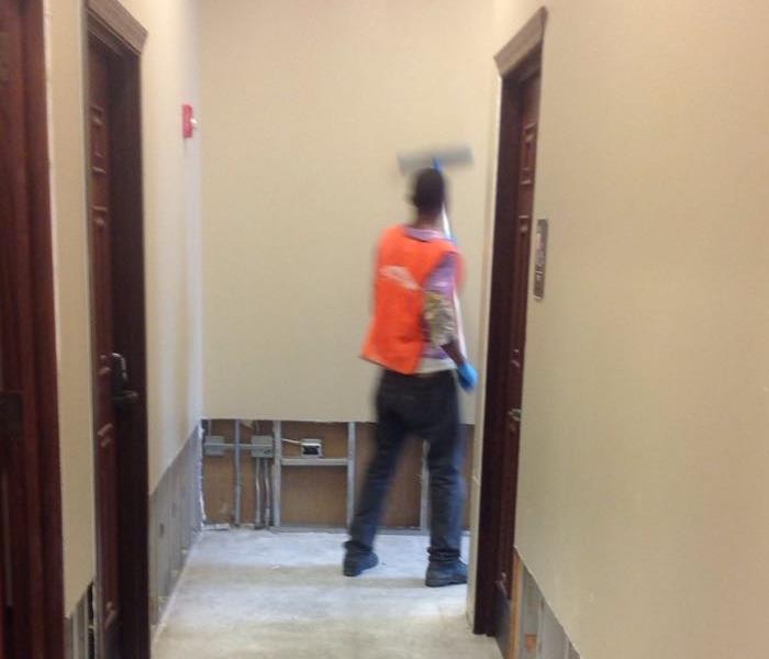 SERVPRO team member in orange vest cleans walls in the hallway of a commercial building. 